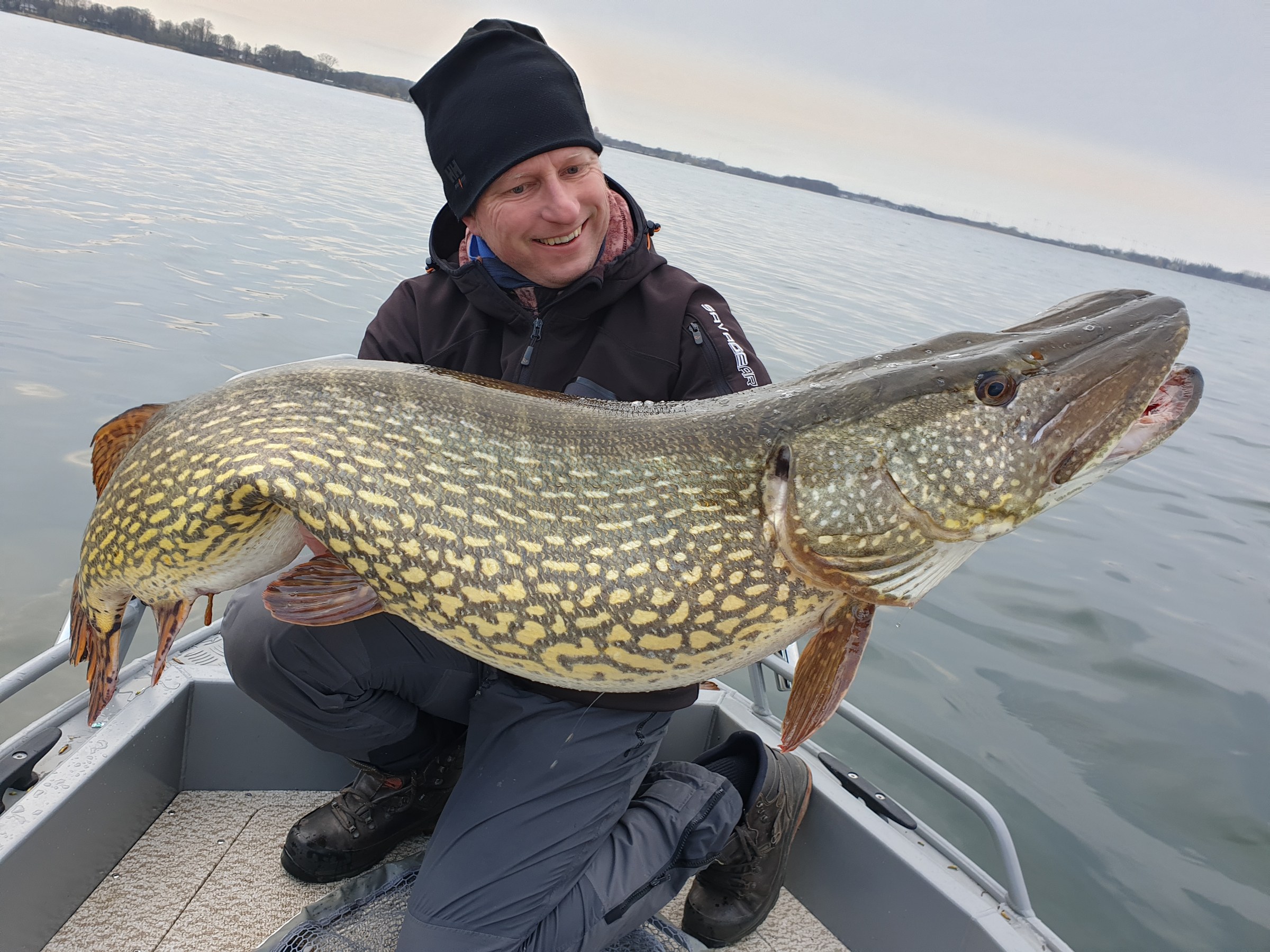 Un pescatore è inginocchiato su una barca e tiene in mano un luccio molto grande