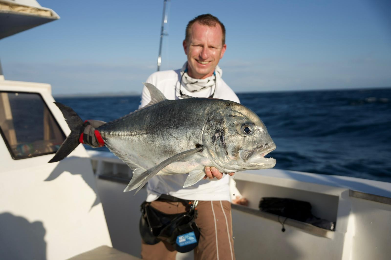 Pescatore su una barca con un grande Giant Trevally argentato