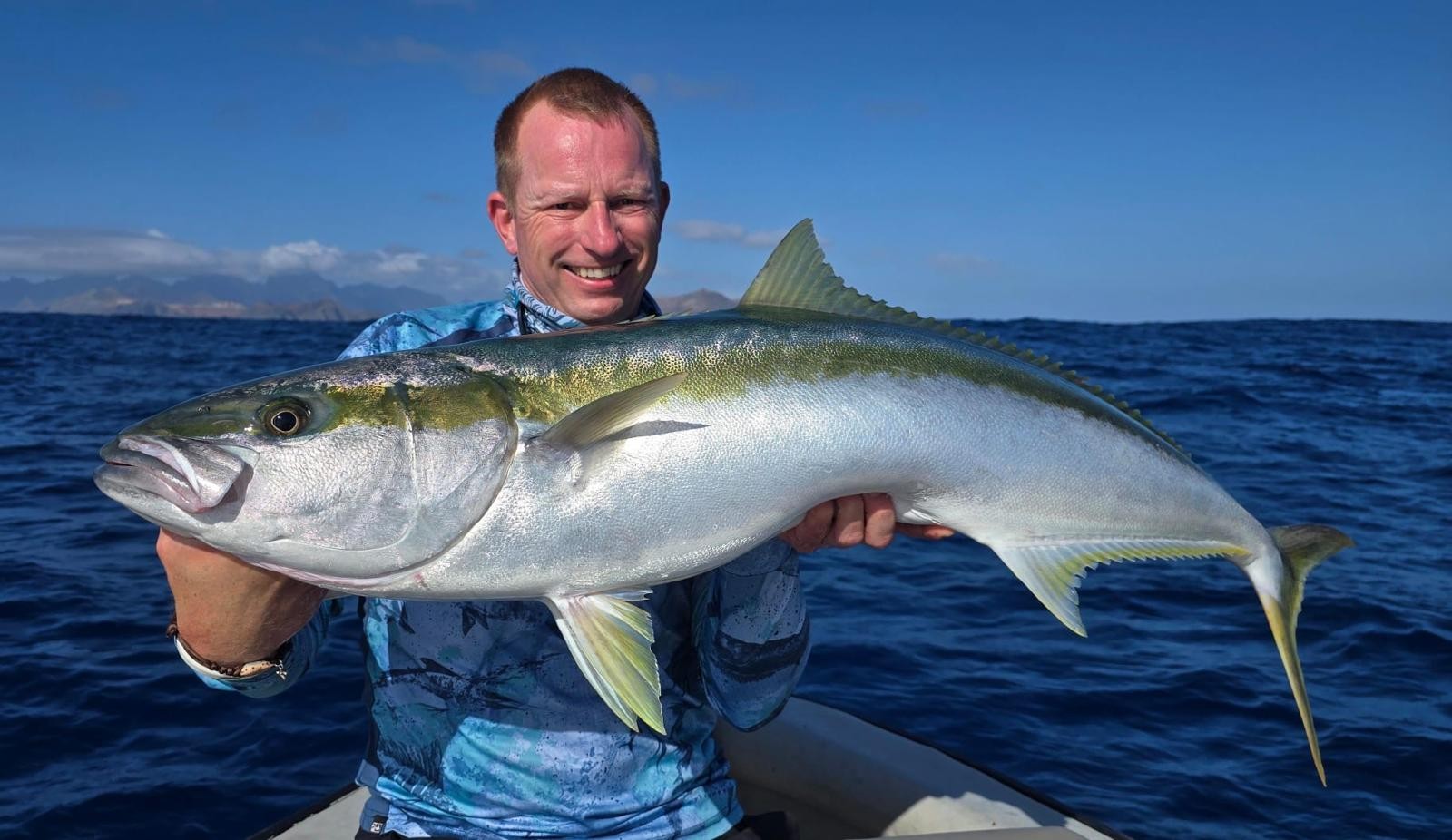 Pescatore su una barca con un grande Yellowtail Kingfish, sullo sfondo mare e isole