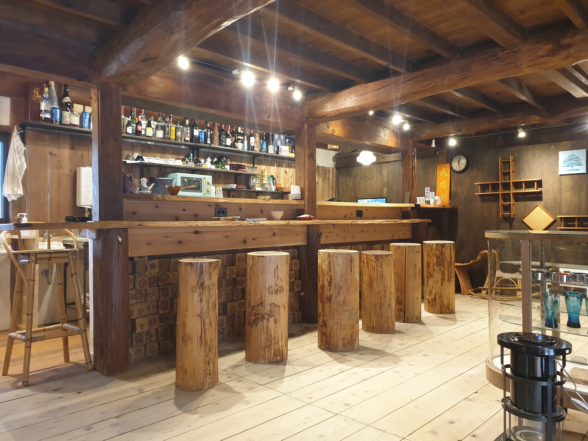 Theke aus Holz mit Hockern aus Baumstämmen und Regalen voller Flaschen