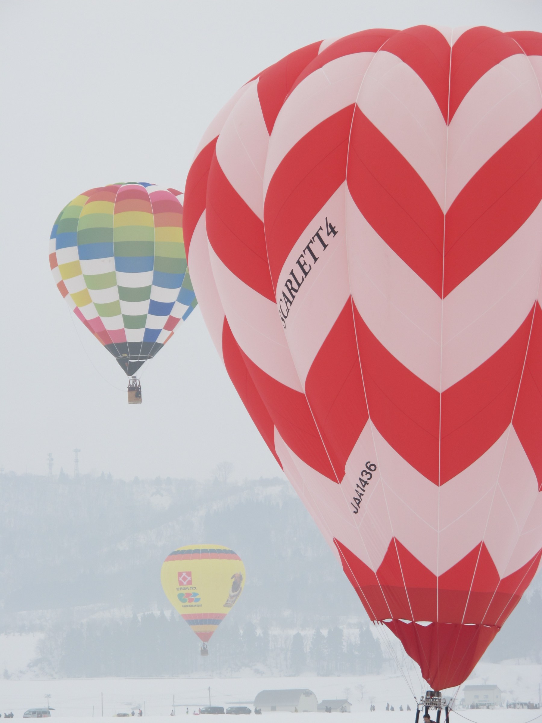 Grande mongolfiera bianca e rossa a zigzag, dietro altre mongolfiere