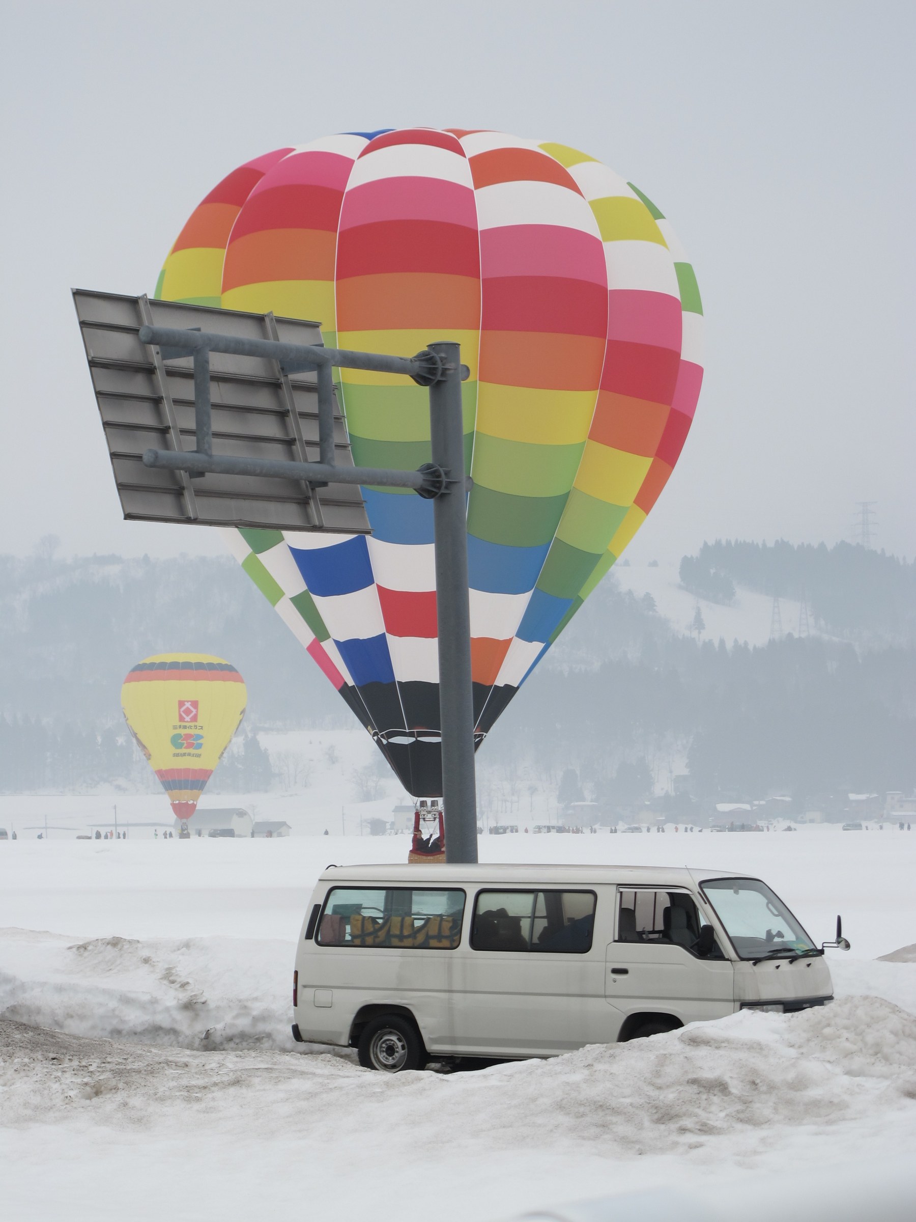 Mongolfiera arcobaleno dietro un cartello, davanti un pulmino bianco nella neve