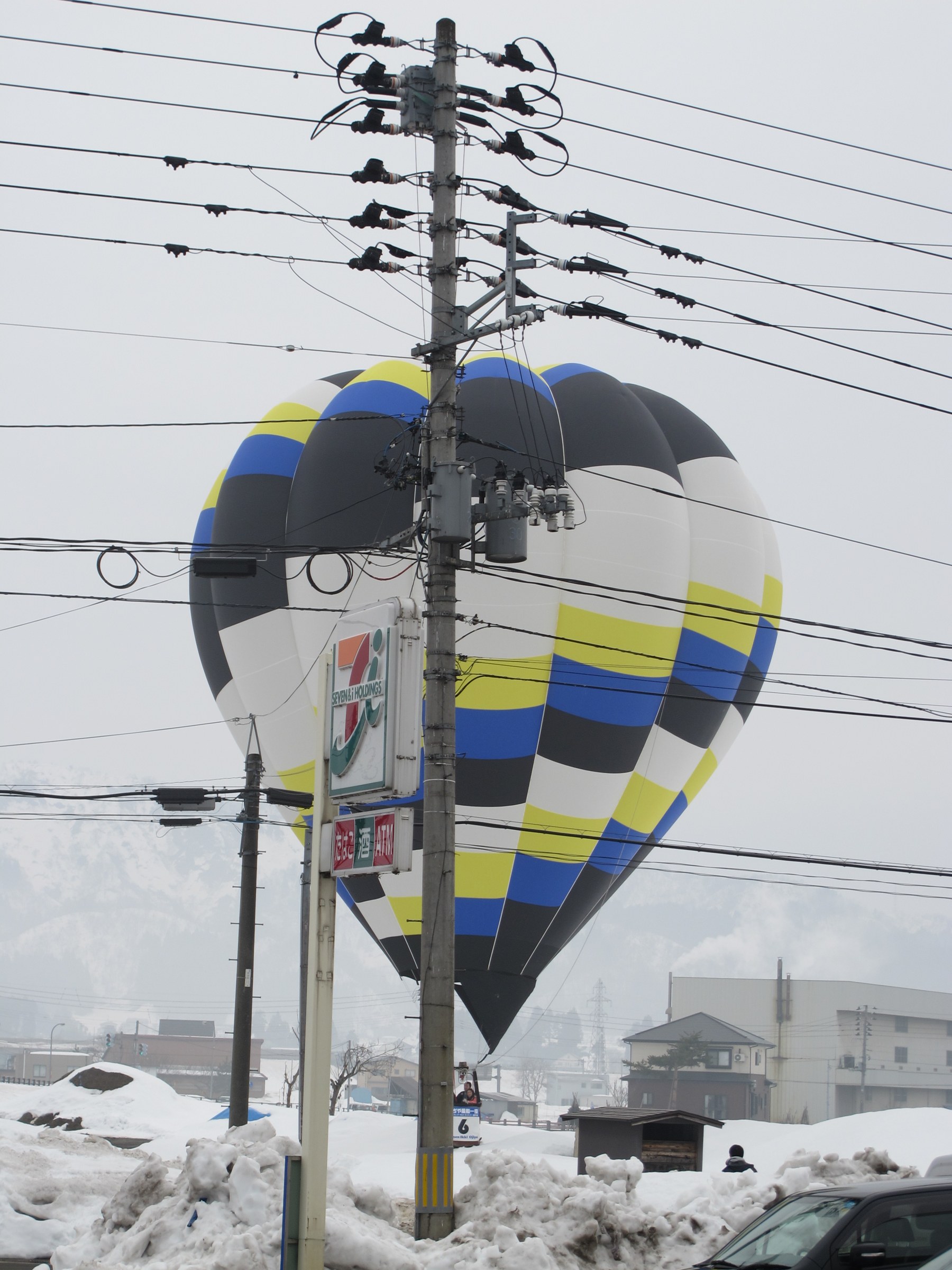 Mongolfiera blu e gialla dietro un palo della luce con l'insegna di un minimarket